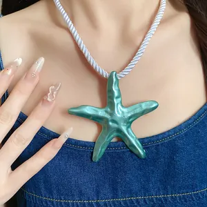 Detail shot of a large teal starfish pendant on a white twisted silk rope necklace on model