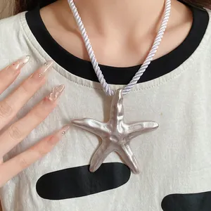 Close-up view of a large silver starfish pendant on a white silk rope cord necklace