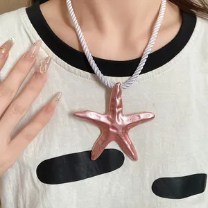 Detail shot of a pink metallic starfish pendant necklace with white twisted silk rope cord.