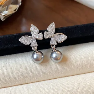 Close-up of dainty butterfly earrings with sparkling stones and grey pearl drops.