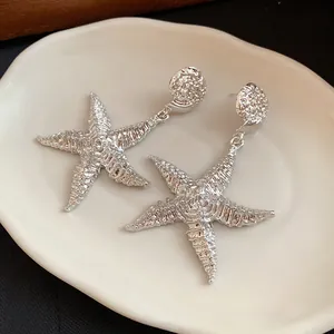 Dettaglio ravvicinato di orecchini pendenti a forma di stella marina in argento testurizzato