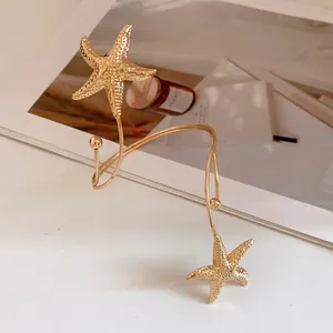 Close-up detail of a gold metal starfish arm cuff bracelet with elegant textured finish