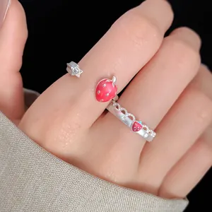 Close-up of a silver open ring featuring red enamel strawberry and star charms on a hand.