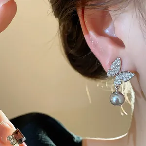 Close-up detail of exquisite butterfly earring with grey pearl drop on an ear model