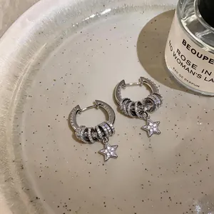 Detailed macro shot of elegant silver hoop earrings with zircon star pendants on ceramic