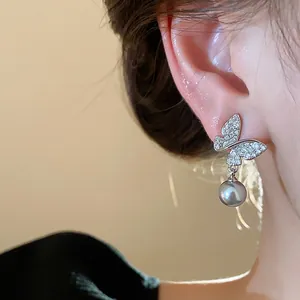 Detailed close-up of refined butterfly stud earrings with a grey pearl drop on a model