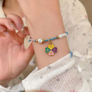 Detailed view of handmade woven bracelet with pearls and four-leaf clover charm
