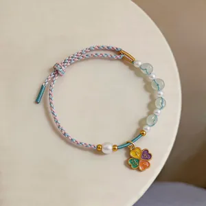 Close-up of handmade woven bracelet with pearls and colorful four-leaf clover charm