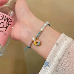 Close-up of a handmade woven bracelet with white pearls and a colorful donut charm
