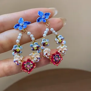 Close-up detail of colorful floral drop earrings with pearls and crystals held in hand