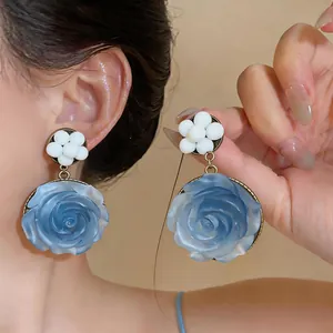 Dettaglio ravvicinato di orecchini pendenti a rosa in resina blu dal design elegante