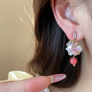 Close-up of 14K gold plated floral earring with sparkling crystals and red bead