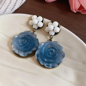Dettaglio di orecchini pendenti a rosa blu in resina stile francese con perline bianche.