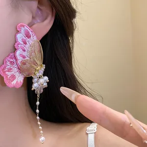 Macro detail of elegant pink embroidered butterfly earrings with pearls and long tassels