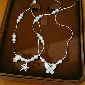 Gros plan d'un collier argenté avec perles et pendentifs étoile et papillon en zircon.