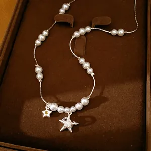Vue détaillée du collier de perles avec étoile en zircon et breloques de planète sur plateau.