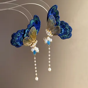 Detail shot of blue embroidered butterfly earrings with pearl tassels and gold accents