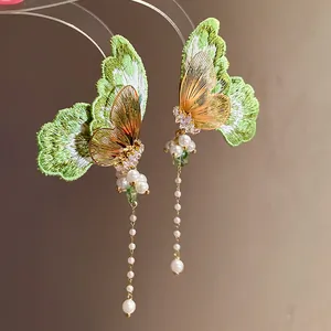 Close-up detail of elegant green embroidery butterfly tassel earrings with pearls.