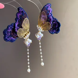 Close-up detail of embroidered butterfly earrings with zircon and pearl tassels.
