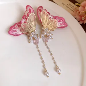 Detailed view of embroidered pink butterfly earrings with pearl tassels and gold accents.