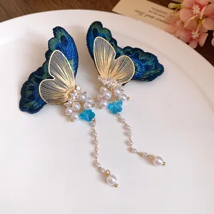 Close-up of butterfly embroidery earrings with long pearl tassels and blue crystals