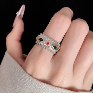 Dettaglio macro di un anello vintage in stile corte con zirconi verdi e rossi su dito