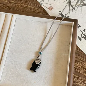 Dettaglio della collana in corda intrecciata con ciondolo a pesce nero e cuore
