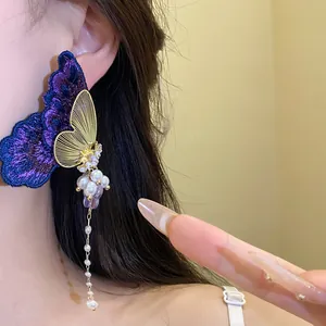 Macro detail of embroidered butterfly earrings with pearl tassel on an ear.