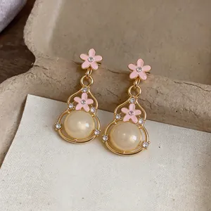 Dettaglio di orecchini a forma di zucca con fiori in smalto rosa e perle di resina