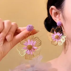 Dettaglio di grandi orecchini a fiore intrecciati a mano viola con petali dorati