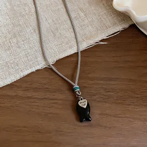 Dettaglio della collana in corda intrecciata con ciondolo a forma di pesce e cuore.