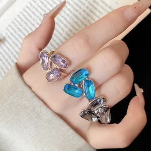 Dettaglio di eleganti anelli aperti con strass ovali viola, blu e grigi indossati sulla mano