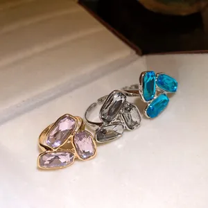 Primo piano di tre anelli regolabili con gemme sfaccettate rosa, grigie e blu.