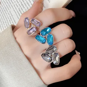 Dettaglio di anelli con strass blu, viola e grigi indossati su una mano.