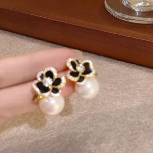 Détail de boucles d'oreilles fleur de camélia noir avec cristaux et perles blanches