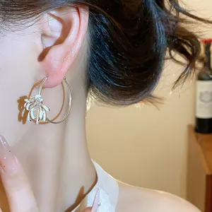 Detail shot of elegant gold hoop earrings with a white enamel floral charm and zircons.