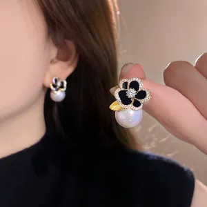 Gros plan de boucles d'oreilles camélia noir avec placage or et détails de perles élégantes.