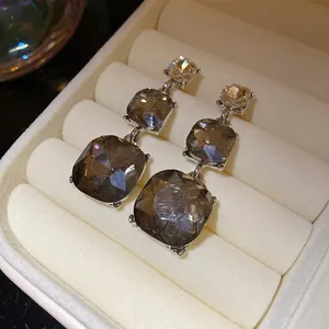 Macro view of tiered drop earrings with faceted smoky grey stones in a cream jewelry box