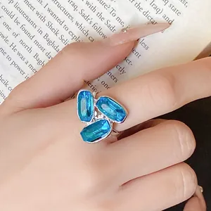 Dettaglio di un anello aperto in argento con tre gemme blu ovali su una mano