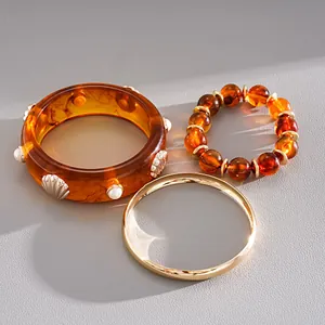 Macro detail of retro 3-piece jewelry set featuring amber resin bangle and gold bracelet