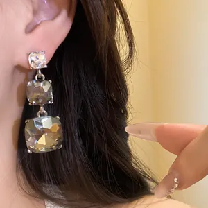 Close-up detail of elegant three-tier square rhinestone drop earrings worn on ear