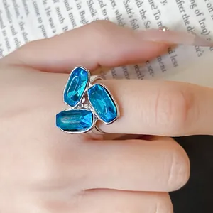 Dettaglio di un anello aperto in argento con tre pietre blu scintillanti sul dito