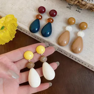 Detailed view of three colorful resin teardrop earrings held by hand over a book