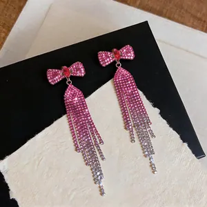Macro detail of elegant pink rhinestone bow earrings with long gradient tassels.