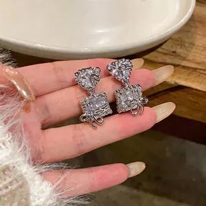 Elegant silver bow earrings with sparkling heart and square zircon stones held on hand