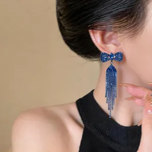 Close-up of blue bowknot earrings with sparkling tassels on an elegant model ear.
