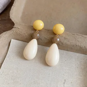 Close-up detail of resin teardrop earrings with yellow spheres and brown faceted beads