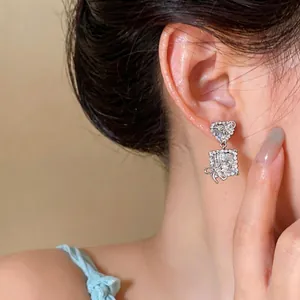 Elegant silver heart and square zircon stud earrings with bow details worn on ear model