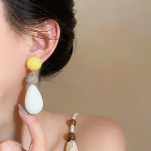 Close-up detail of colorful resin waterdrop dangling earrings worn on ear by model