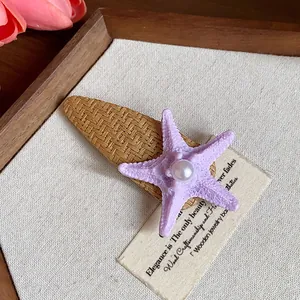Close-up of a bohemian purple starfish hair clip with a central pearl on a straw base